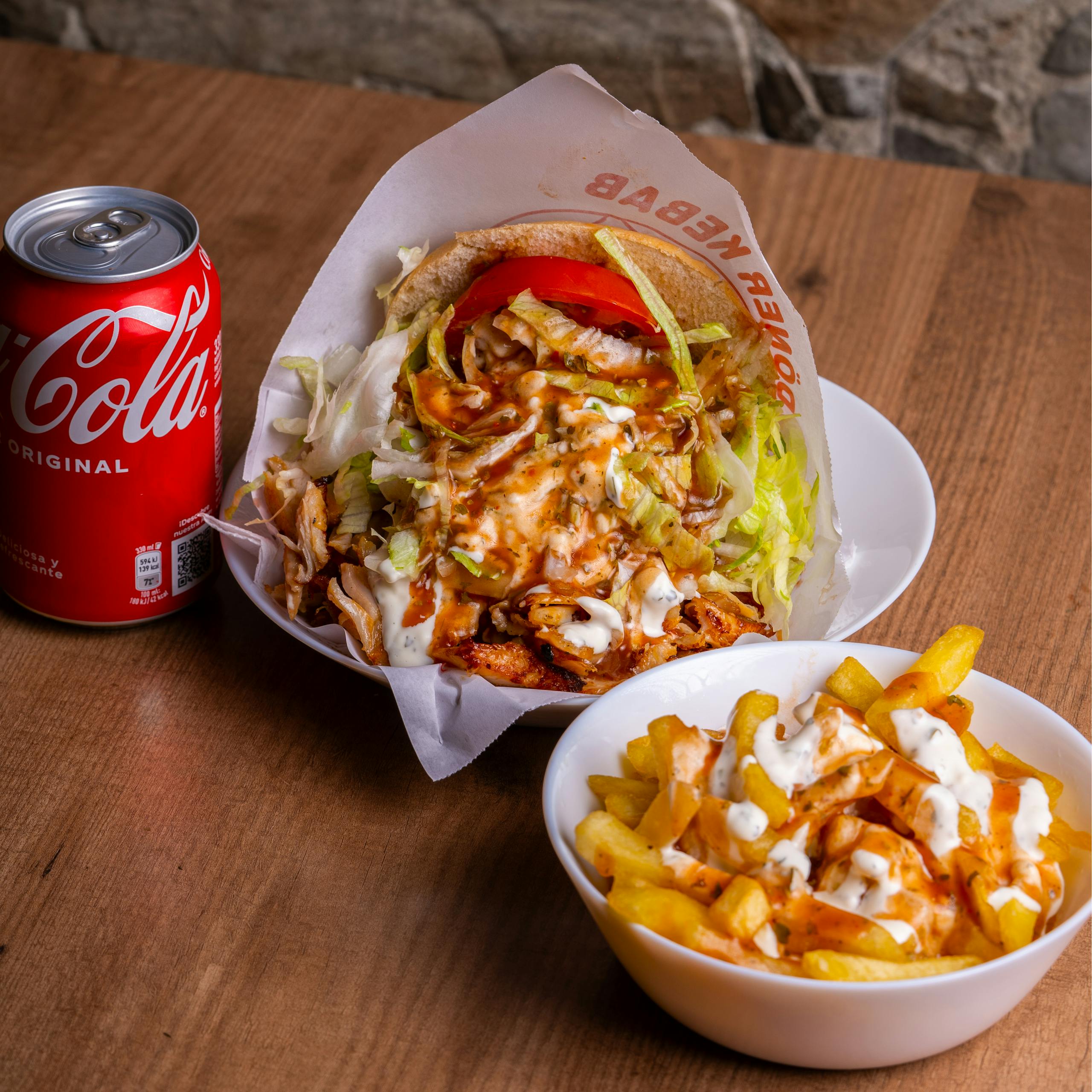 A tempting doner kebab with fries and a refreshing cola on a wooden table.