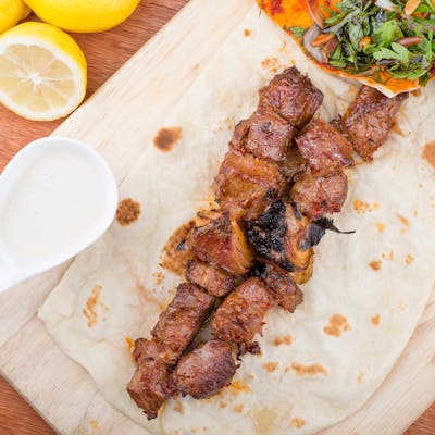 Close-up of grilled kebab on flatbread with fresh salad, lemon, and sauce.