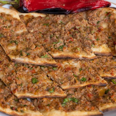 Close-up of traditional Turkish Lahmacun with fresh toppings on a white ceramic plate.