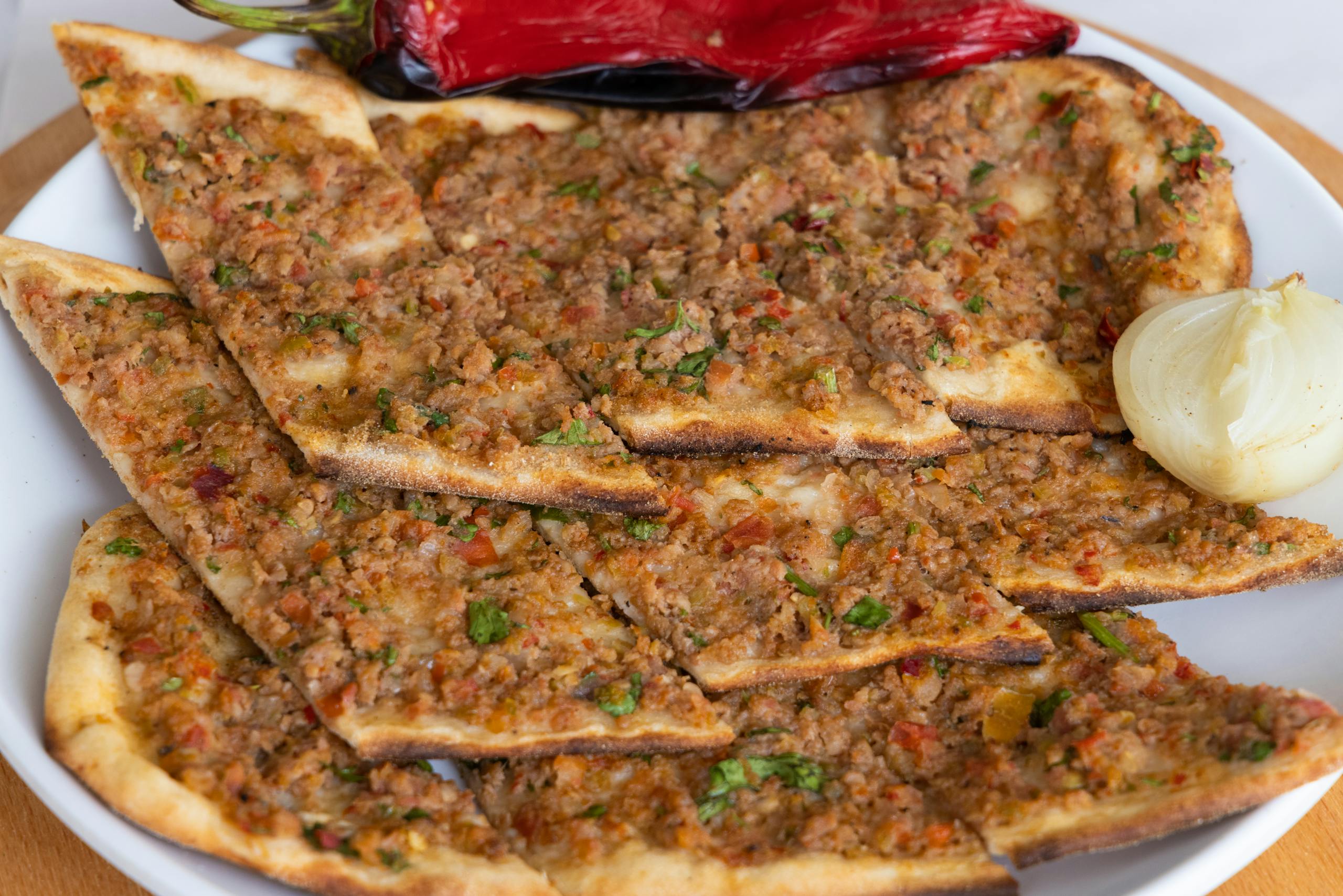 Close-up of traditional Turkish Lahmacun with fresh toppings on a white ceramic plate.