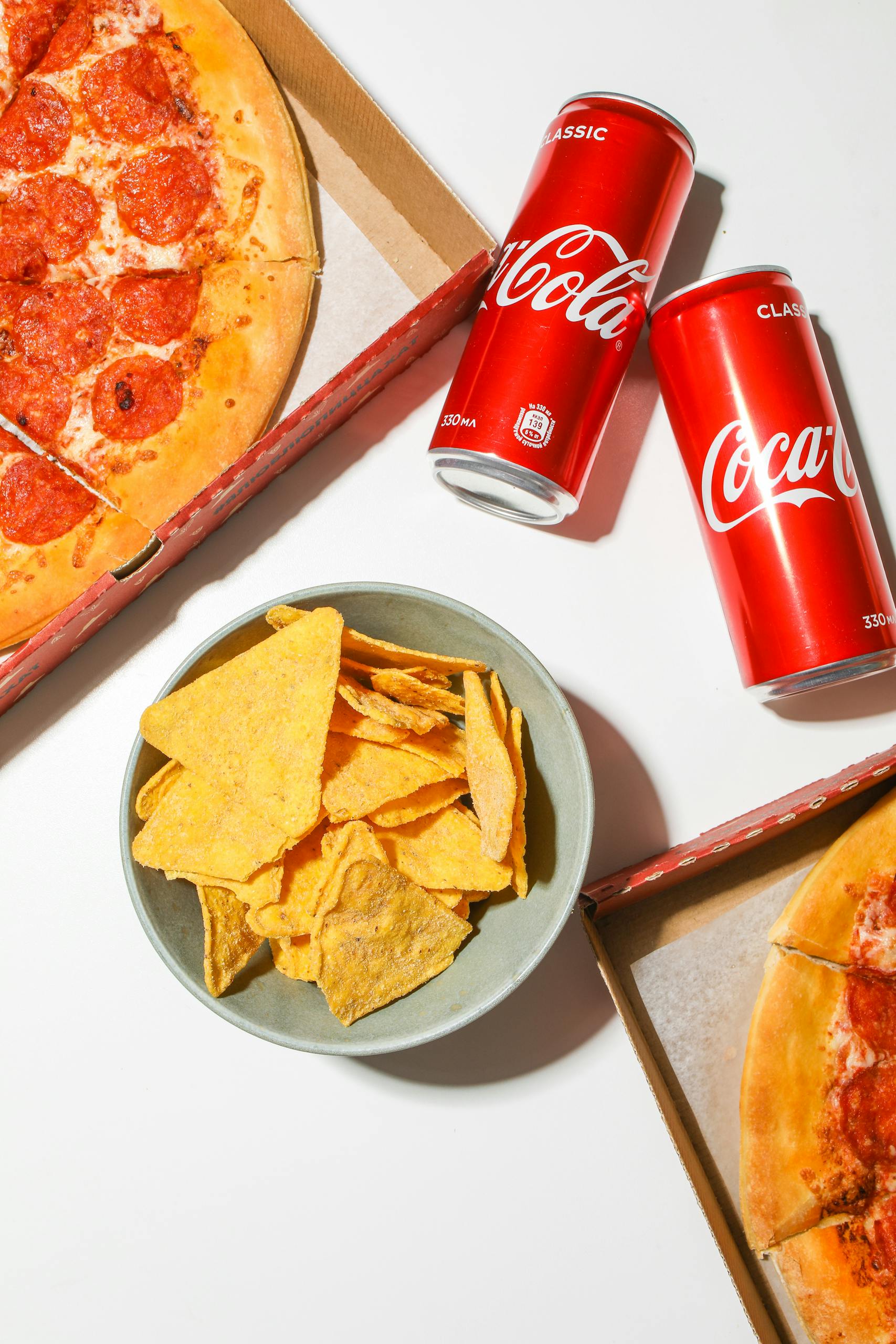 Delicious pepperoni pizza, cola cans, and chips on a white background. Perfect for a snack spread.